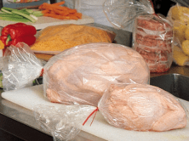 A table with meat and vegetables wrapped in plastic.